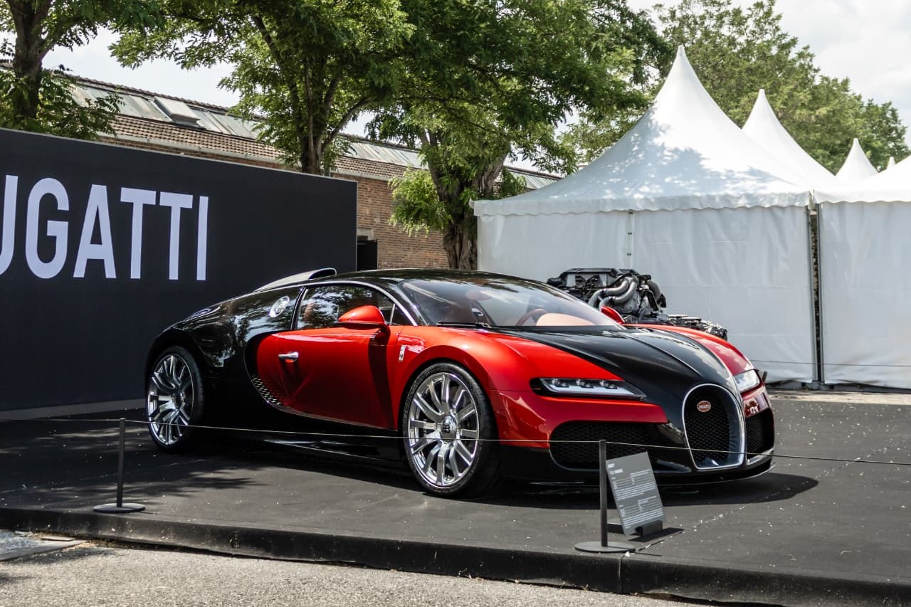 Bugatti Veyron « FKP Hommage » rouge et noire en trois-quarts avant devant le panneau BUGATTI au Concours International d'Élégance Schlumpf
